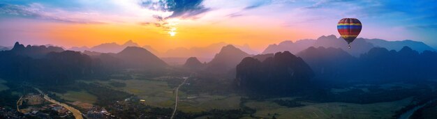 Luftaufnahme von Vang Vieng mit Bergen und Ballon bei Sonnenuntergang.