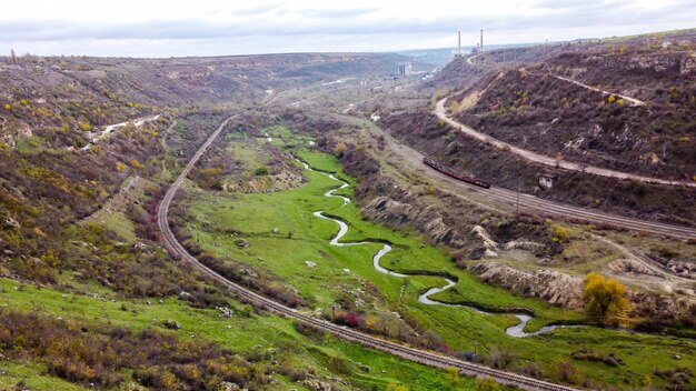 Luftdrohnenansicht der Natur in Moldawien, strömen Sie den Strom, der in die Schlucht fließt, Hänge mit spärlicher Vegetation und Felsen, beweglicher Zug, bewölkter Himmel