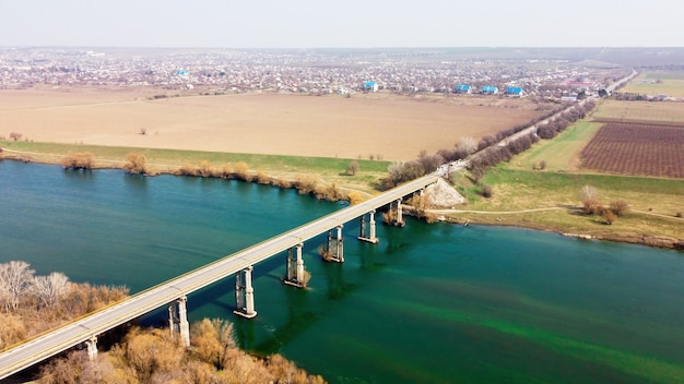 Luftdrohnenansicht einer Brücke über den schwimmenden Fluss und das nahe gelegene Dorf, Felder, Nebel in der Luft, Moldawien