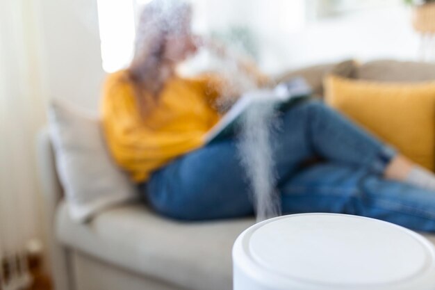 Luftreiniger in gemütlichem Weiß Wohnzimmer zum Filtern und Reinigen Staub entfernen PM25 HEPA zu Hause mit Frau, die ein Buch auf dem Sofa liest, für frische Luft und gesundes Leben Luftverschmutzungskonzept