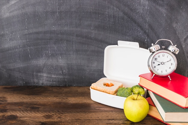 Lunchbox und Apfel in der Nähe von Büchern und Wecker