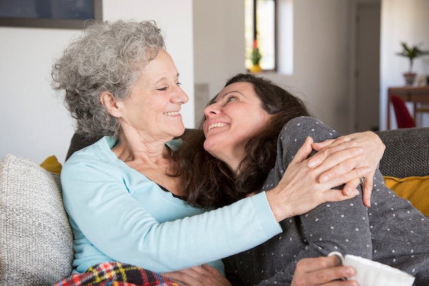 Lustige ältere Mutter und ihre Tochter, die sich zu Hause auf Sofa entspannt