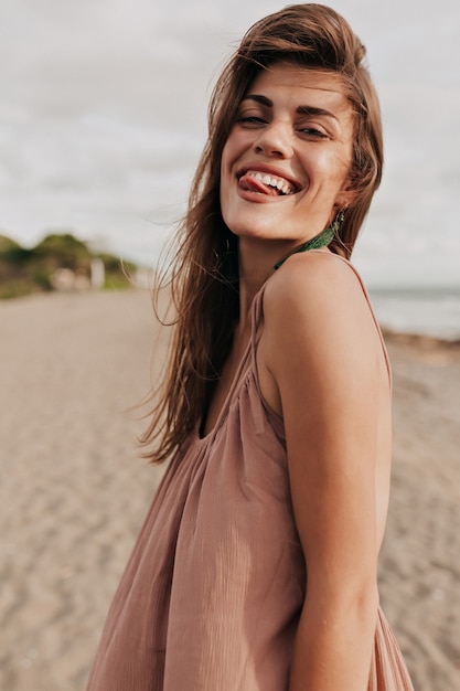 Lustige charmante dame mit braunen haaren macht gesichter und spaß am strand im sonnenlicht