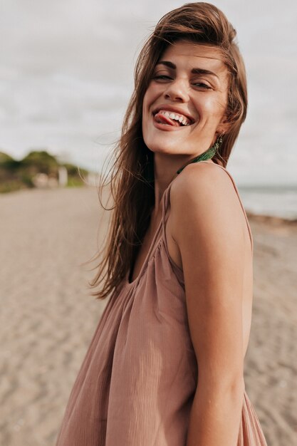 Lustige charmante Dame mit braunen Haaren macht Gesichter und Spaß am Strand im Sonnenlicht