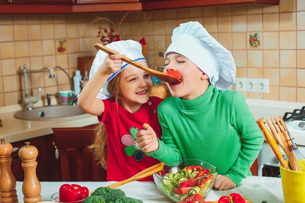 Lustige Familienkinder bereiten den frischen Gemüsesalat in der Küche vor