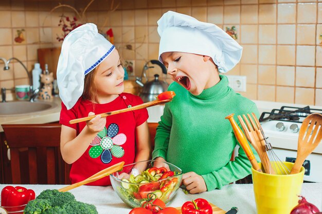 Lustige Familienkinder bereiten einen frischen Gemüsesalat in der Küche vor
