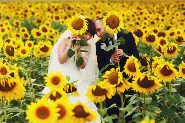Lustige Haltung des verheirateten Paars auf dem Feld, das Sonnenblumen hält