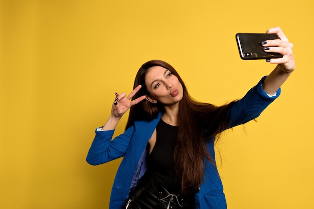 Lustige hübsche Frau mit dem langen dunklen Haar, das mit küssendem Gesichtsausdruck aufwirft. Kaukasisches Mädchen macht ein Selfie.