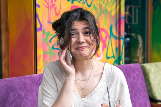 Lustige junge Frau, die am Telefon mit einem Glas Limonade spricht