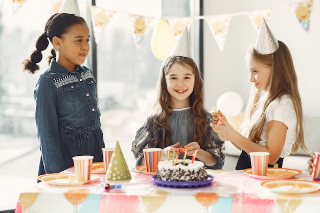 Lustige Kindergeburtstagsfeier im dekorierten Raum. Glückliche Kinder mit Kuchen und Luftballons.