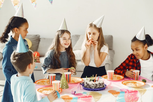 Lustige Kindergeburtstagsfeier im dekorierten Raum. Glückliche Kinder mit Kuchen und Luftballons.