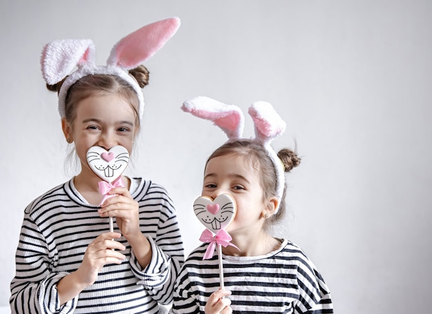 Lustige kleine Mädchen mit Osterohren auf ihren Köpfen und Ostern Lebkuchen auf Stöcken.