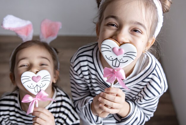 Lustige kleine Schwestern mit Osterlebkuchen in Form von Hasengesichtern und mit Hasenohren.