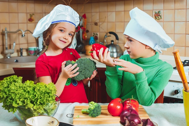 Lustige lustige Kinder der Familie bereiten den frischen Gemüsesalat in der Küche vor