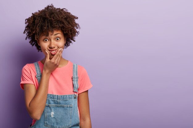 Lustige schöne junge Frau mit einem Afro, der im Overall aufwirft