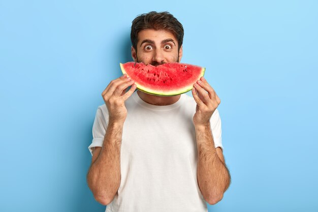 Lustiger Mann an einem Sommertag, der eine Scheibe Wassermelone hält