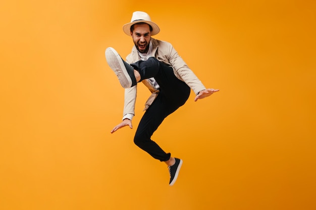 Lustiger Mann mit Hut springt auf orangefarbenem Hintergrund