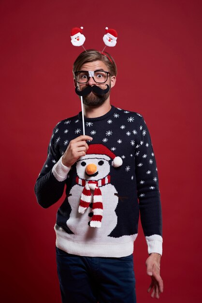 Lustiger Mann mit Schnurrbartmaske gekleidet in Weihnachtskleidung
