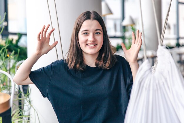 Lustiger Teenager sitzt in einer Hängematte in einem schwarzen T-Shirt