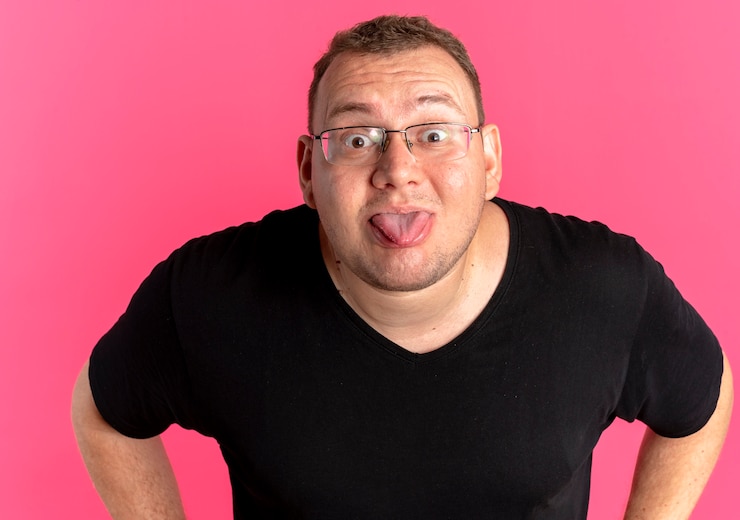 Kostenlose Foto lustiger übergewichtiger mann in der brille, die das schwarze t-shirt trägt, das zunge heraussteht, die über rosa wand steht