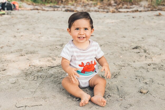 Lustiges Baby, das auf sandigem Strand sitzt