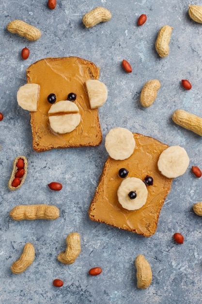 Lustiges Bären- und Affengesichtssandwich mit Erdnussbutter, Banane und schwarzer Johannisbeere, Erdnüsse, Draufsicht