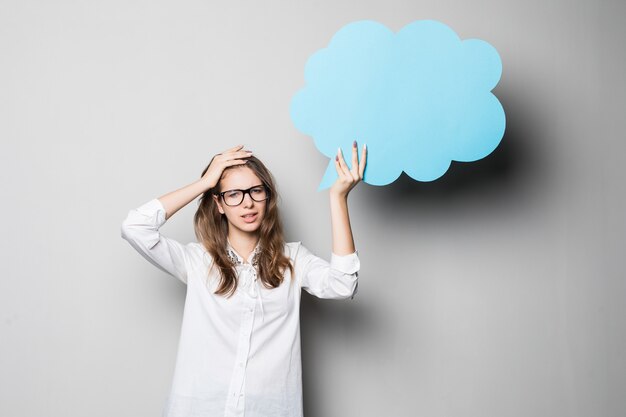 Lustiges junges hübsches Studentenmädchen hält blaue Chatwolken über ihrem Kopf lokalisiert auf weißem Hintergrund