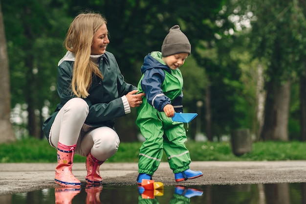 Lustiges Kind in den Regenstiefeln, die in einem Regenpark spielen