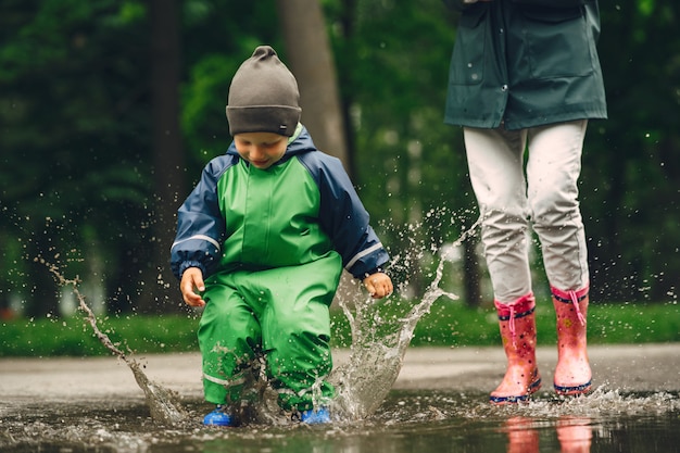 Lustiges Kind in den Regenstiefeln, die in einem Regenpark spielen