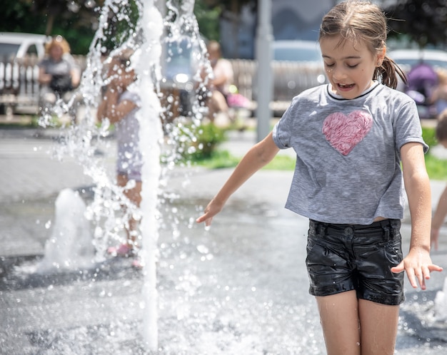 Kostenloses Foto lustiges kleines mädchen in einem brunnen, unter den wasserspritzern an einem heißen sommertag.