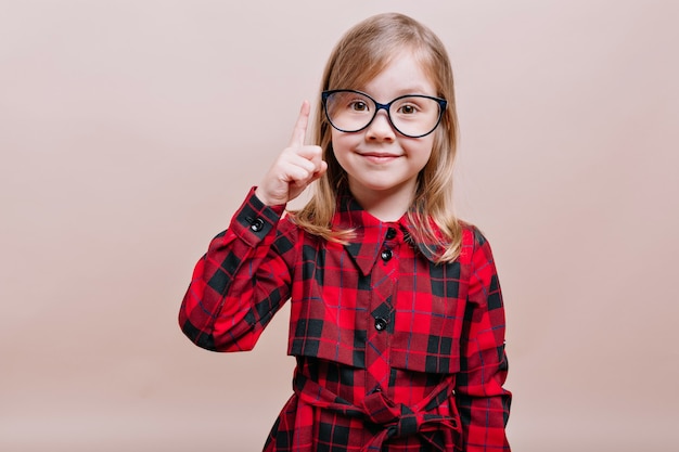 Lustiges kluges kleines Mädchen trägt Brille und kariertes Hemd, hob einen Finger und lächelt vorne