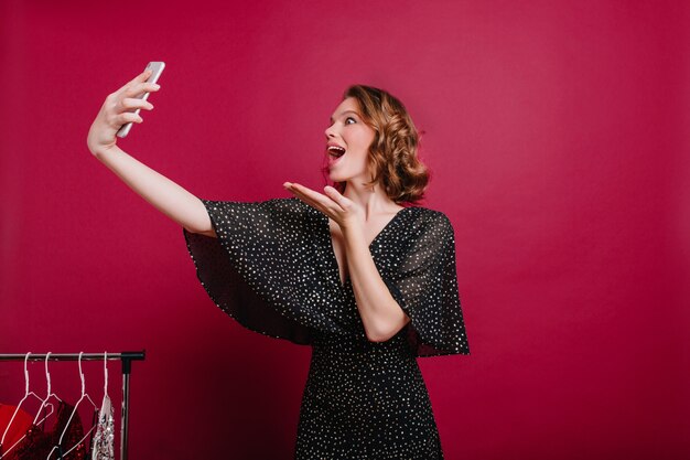 Lustiges Mädchen trägt Retro schwarzes Kleid, das Selfie in ihrem Zimmer macht