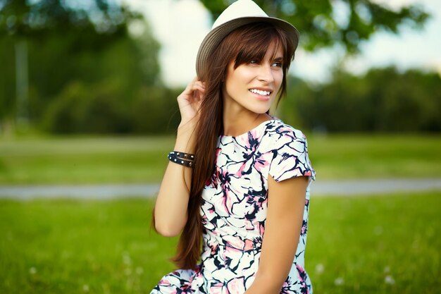 Lustiges stilvolles lächelndes schönes junges Frauenmodell im hellen Sommerkleid des Hutes im Hut im Park