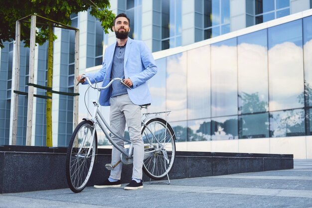 Luxuriöser bärtiger Mann mit Sonnenbrille auf einem Fahrrad in einer Innenstadt.