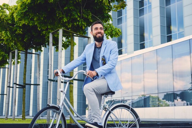 Luxuriöser bärtiger Mann mit Sonnenbrille auf einem Fahrrad in einer Innenstadt.