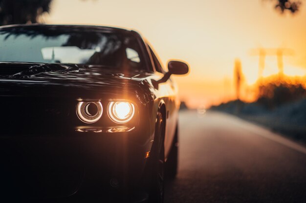 Luxuriöses Auto, das bei Sonnenuntergang mit einem beleuchteten Scheinwerfer auf der Autobahn geparkt ist