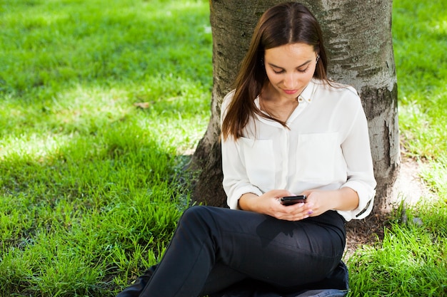 Mädchen arbeitet mit ihrem Telefon unter dem Baum