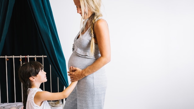 Kostenloses Foto mädchen auf dem rührenden bauch des betts der mutter