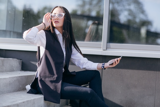 Mädchen auf der Treppe mit einem mobilen in der Hand und berührt ihre Brille