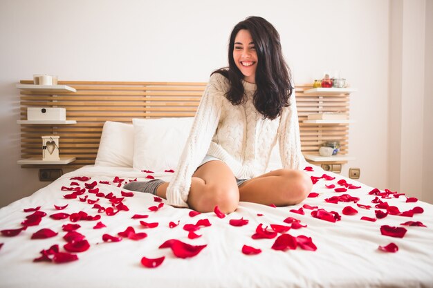 Mädchen auf Knien sitzt auf einem Bett mit den Blumenblättern