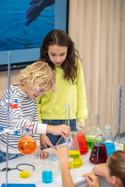 Mädchen beobachtet Jungen, der Pipette in Kolben senkt