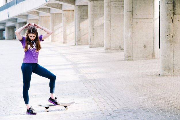 Mädchen berührt ihr Haar und hält ihr Skateboard mit einem Fuß