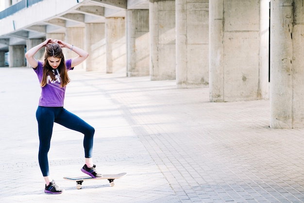 Mädchen berührt ihr Haar und hält ihr Skateboard mit einem Fuß