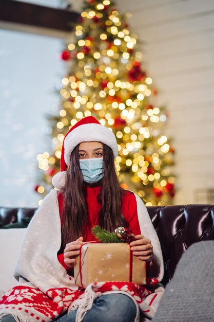 Mädchen, das an Silvester ein Weihnachtsgeschenk hält. Mädchen, das die Kamera betrachtet. Weihnachten während des Coronavirus, Konzept