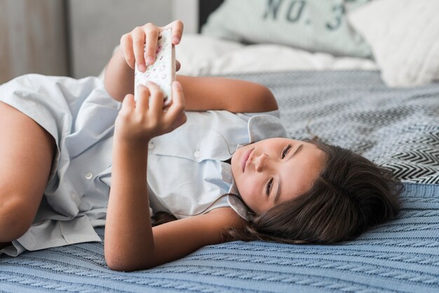 Mädchen, das auf Bett unter Verwendung des intelligenten Telefons liegt