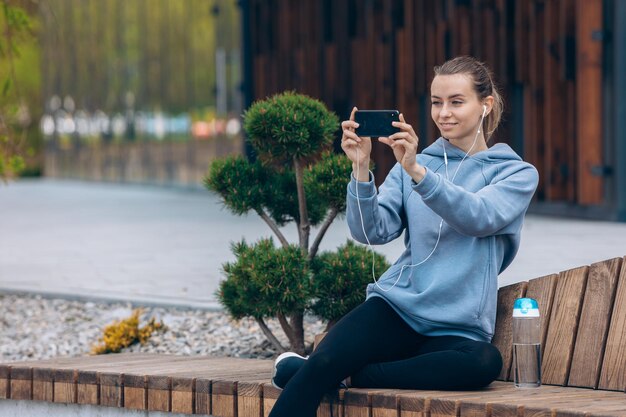 Mädchen, das auf dem Bein auf der Bank sitzt und ein Selfie macht