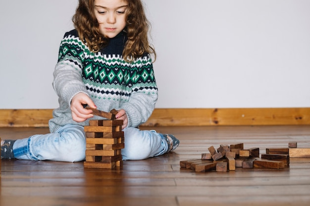 Mädchen, das auf dem Boden spielt jenga Spiel sitzt