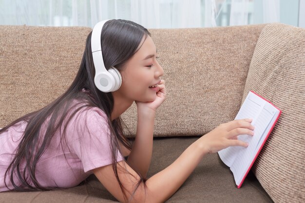 Mädchen, das auf der Couch hört Musik und liest Bücher liegt.