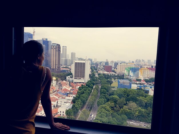Mädchen, das aus Fenster-Stadt-Stadtbäumen heraus schaut