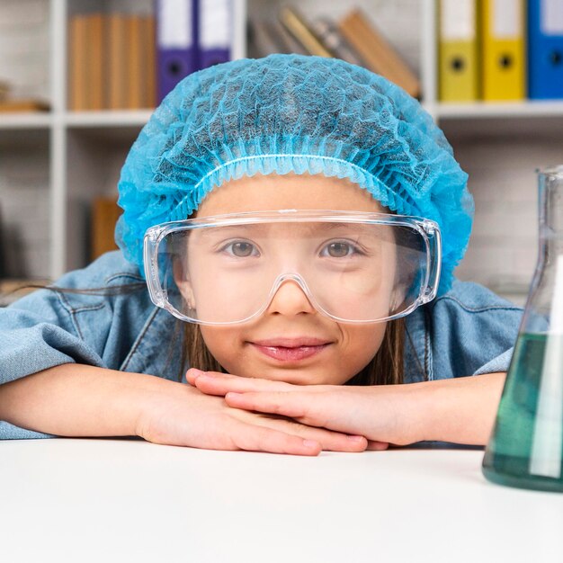 Mädchen, das beim Tragen des Haarnetzes und der Schutzbrille für wissenschaftliche Experimente aufwirft